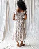 Woman wearing a floral dress standing against a white curtain