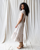 Woman wearing a white and brown floral dress against a white curtain background