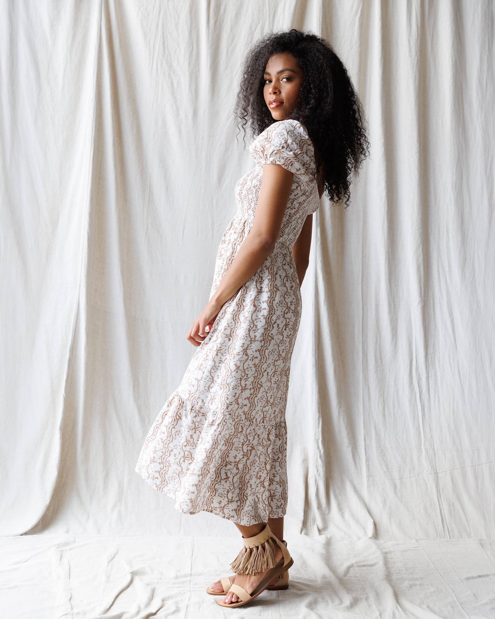 Woman wearing a white and brown floral dress against a white curtain background